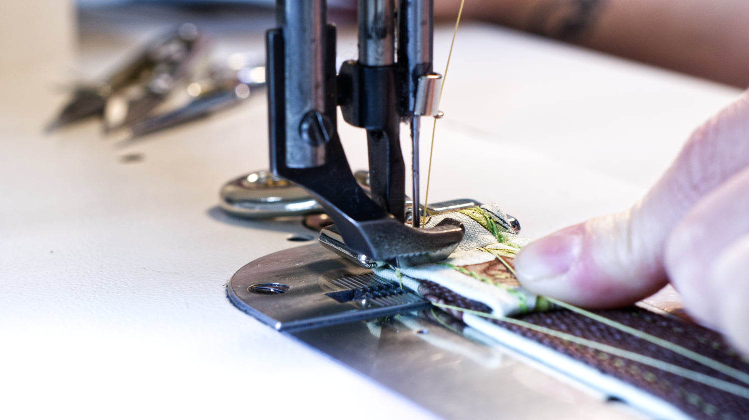 Close up image of a light colored dog leash being stitched between the walking foot of a cream colored juki sewing machine by the fingers of SLiK Hound's Master craftsmen. No pet product is made to a higher standard than SLiK Hound.