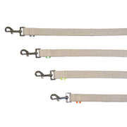 A collection of hemp dog leashes with metal hooks and reflective tabs, laid out in a row. Each are Tan undyed and natural hemp Canvas with different color reflective tabs at all ends, yellow kevlar stitching and shiny silver metal hardware. pictured with white backdrop.